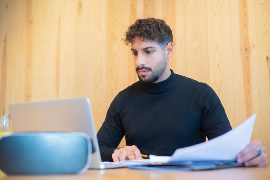 A self-employed man reviewing paperwork on a laptop while comparing health insurance for self employed men